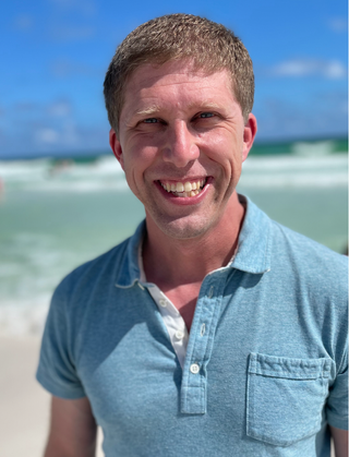 A head shot of Dr. Christopher Jenson standing on a beach.