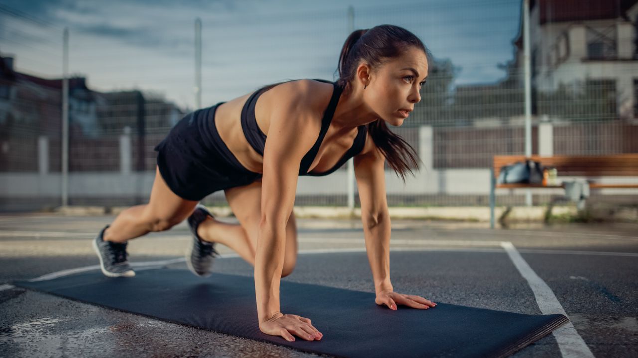 A woman performing mountain climbers on a yoga mat outside 