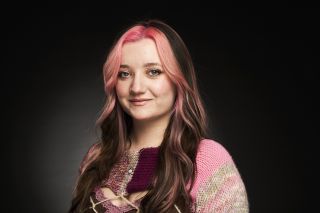 Saphron against a black background with two pink stripes in her hair