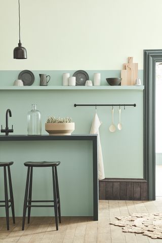 Two shades of green painted on kitchen walls and cabinetry, with open shelving and black bar stools.