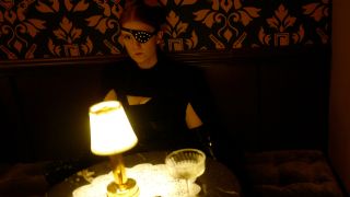 A mysterious woman with an eyepatch sits at a dimly lit table in The Continental.