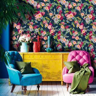 Bold living room with dark floral wallpaper, yellow sideboard and accent armchairs in blue and pink