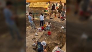 A group of archaeologists excavates under a tent.