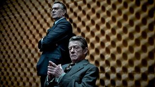 Gary Oldman and John Hurt stand near a spongey, soundproof wall wearing suits in a still from Tinker Tailor Soldier Spy
