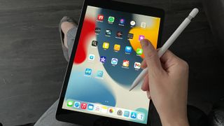 En person sitter med en iPad 10.2 (2021) i knät, redo att börja anteckna med en tillhörande stylus.