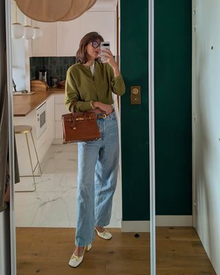 Woman wearing olive green sweater and jeans.