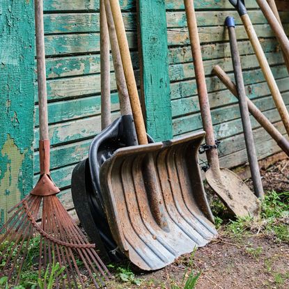 A row of gardening tools leaning against a wall with peeling paint