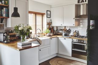 L-shape white kitchen with oak worktops, black pendant light and rugs