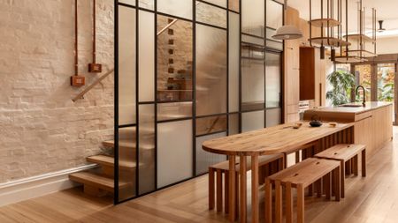 A bright and airy open concept dining room and kitchen drenched in wood and a stained glass wall by a staircase
