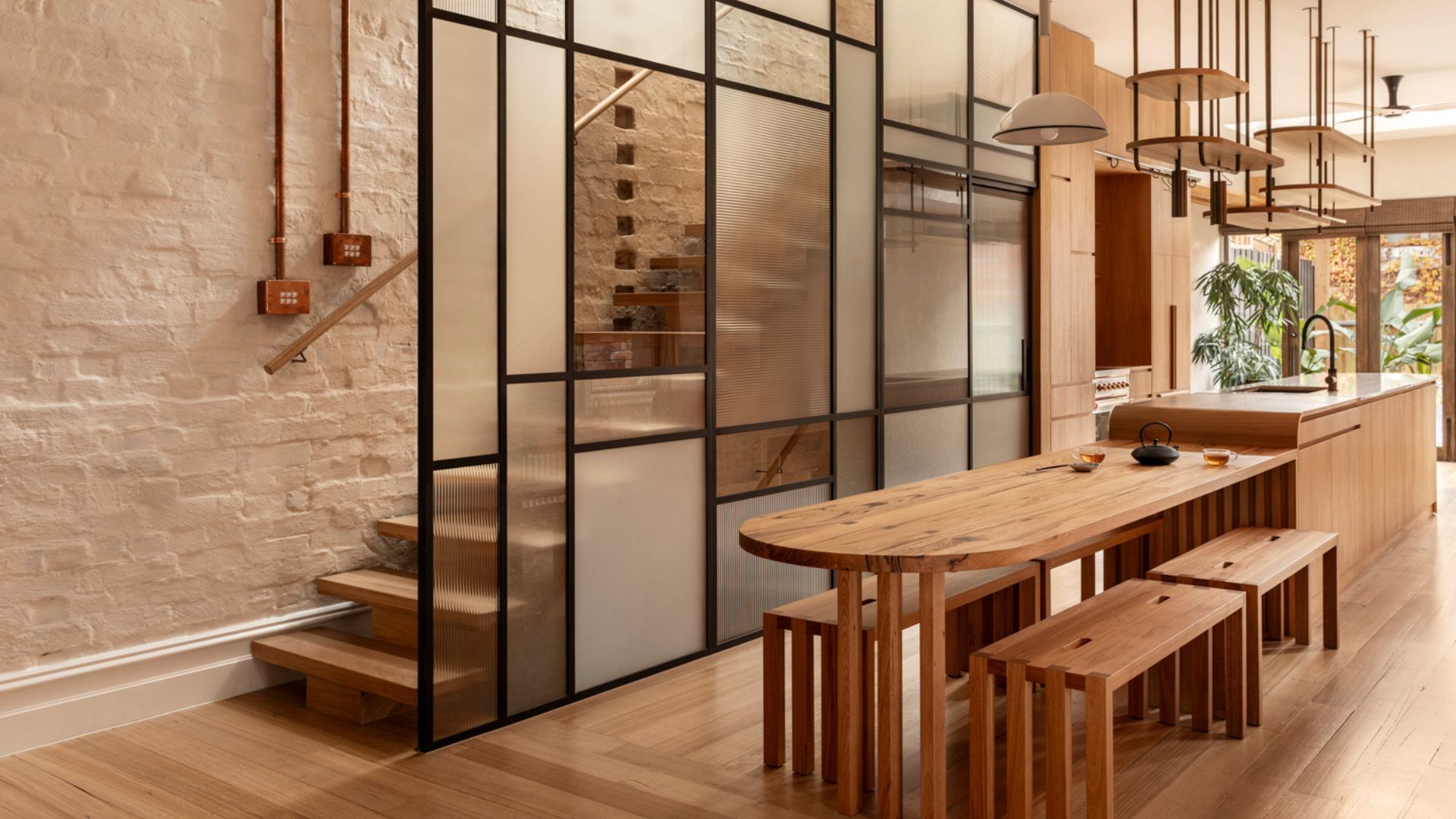 A bright and airy open concept dining room and kitchen drenched in wood and a stained glass wall by a staircase