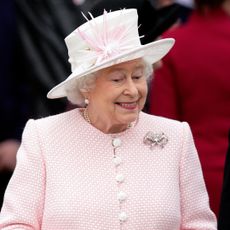 Queen Elizabeth wears a pink jacket featuring white buttons, and a white hat with pink detailing