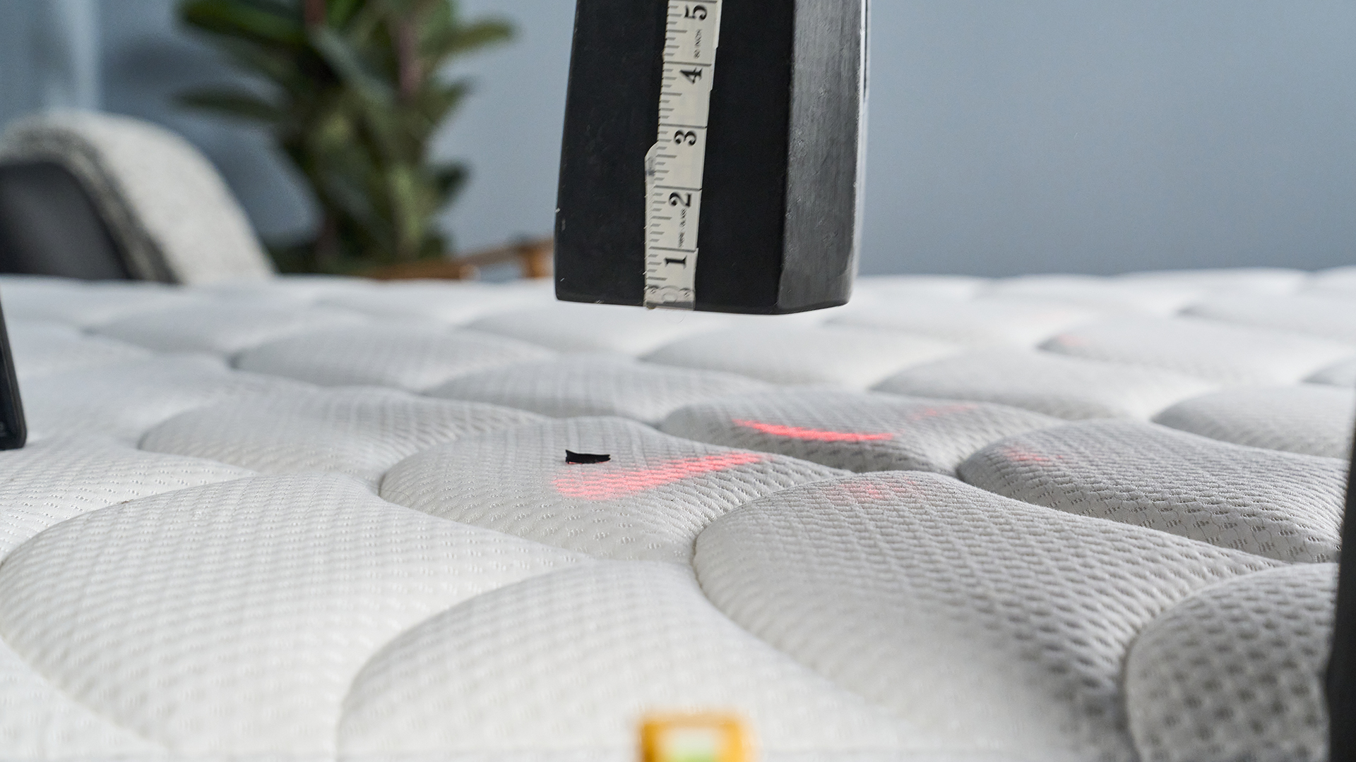 A black 25kg weight with a measuring tape on its side being lifted off the cloud-like surface of the DreamCloud Classic mattress to measure how quickly the mattress responds and returns to its original height