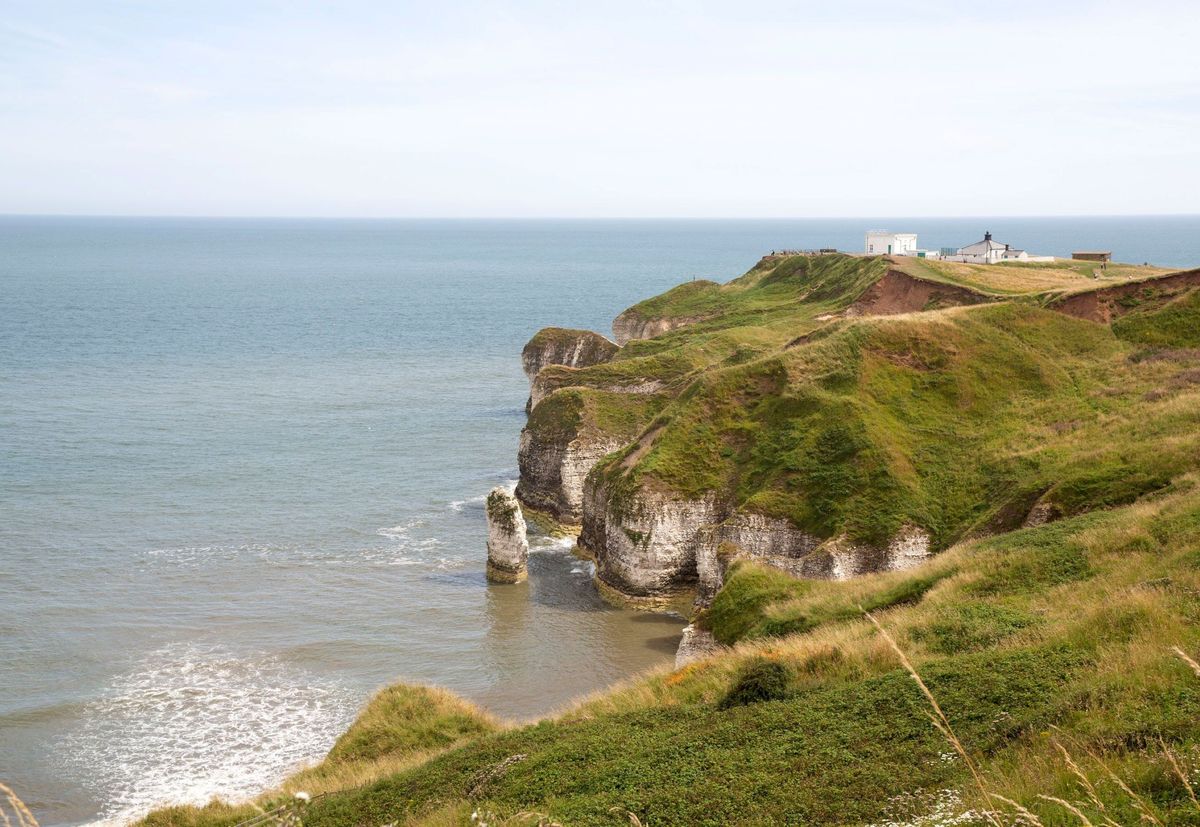 The coastal site of the build with grass covered headland and a lighthouse