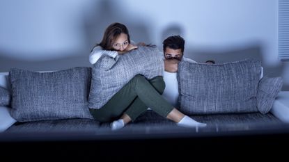 Young smiling couple watching a scary movie at home. Both Caucasian, casual, about 20 years old.
