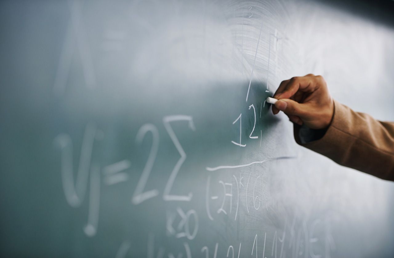 Cropped image of a teacher writing a formula on a blackboard