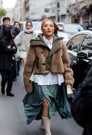 woman wearing a teddy jacket, button-down shirt, denim skirt, and boots