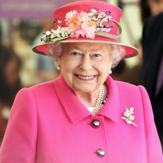 Queen Elizabeth wears a bright pink coat and matching hat adorned with flowers