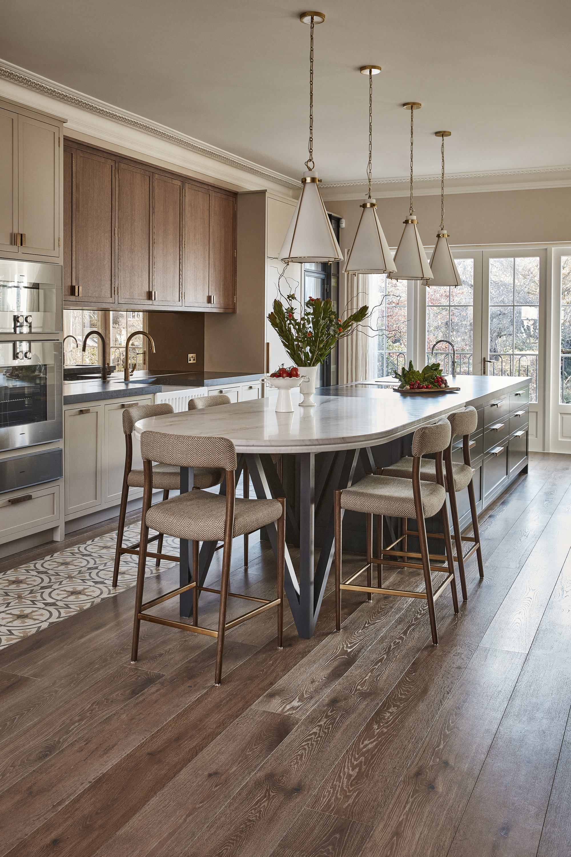 A modern kitchen/dining space with a large kitchen island, wooden cabinetry, and dark wooden floorboards with an integrated tile area running along the kitchen workspace