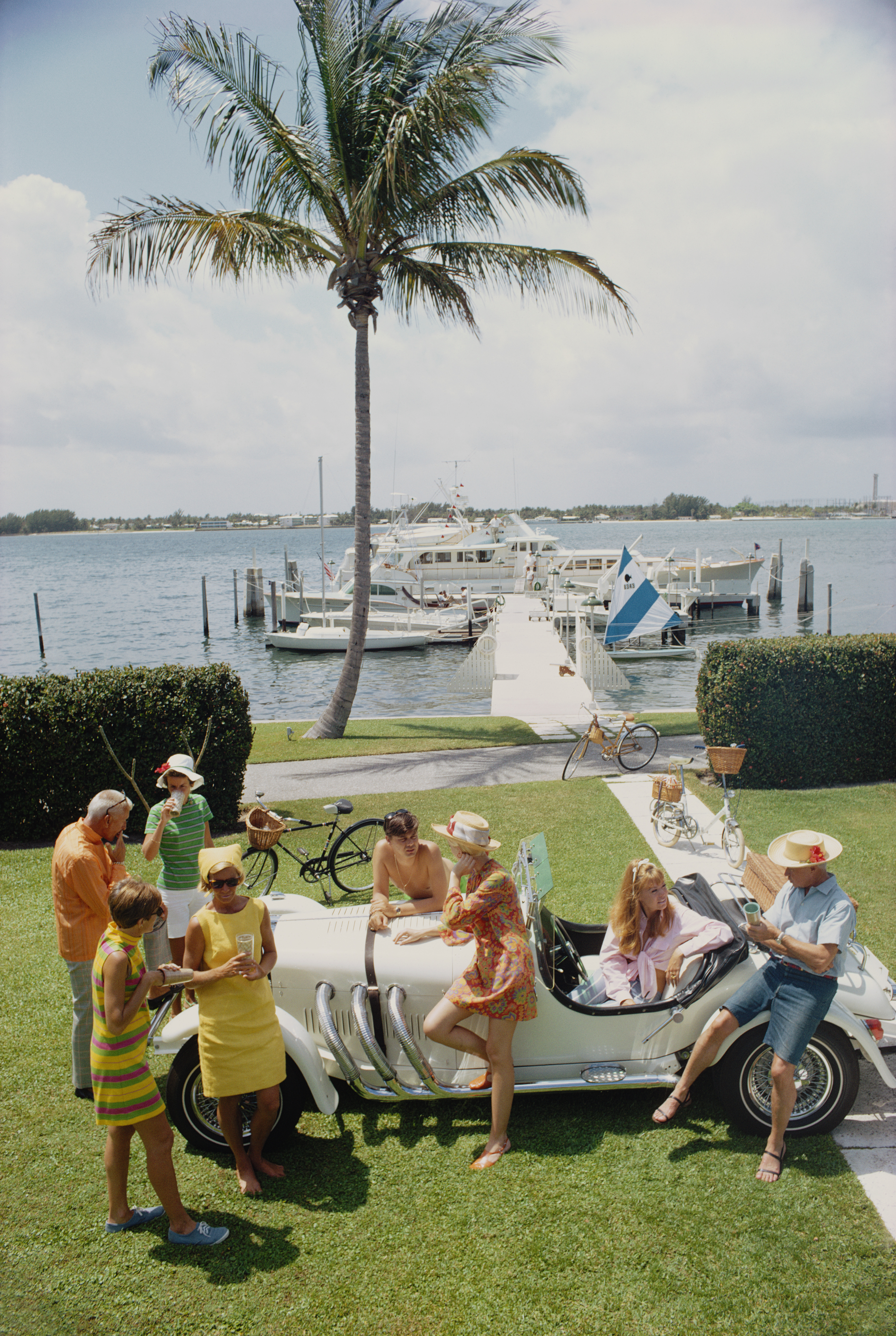 A group of people dressed in summer clothes surrounding a vintage open-top car
