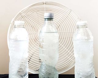 Three bottles of water in safe distance from electric fan to cool room