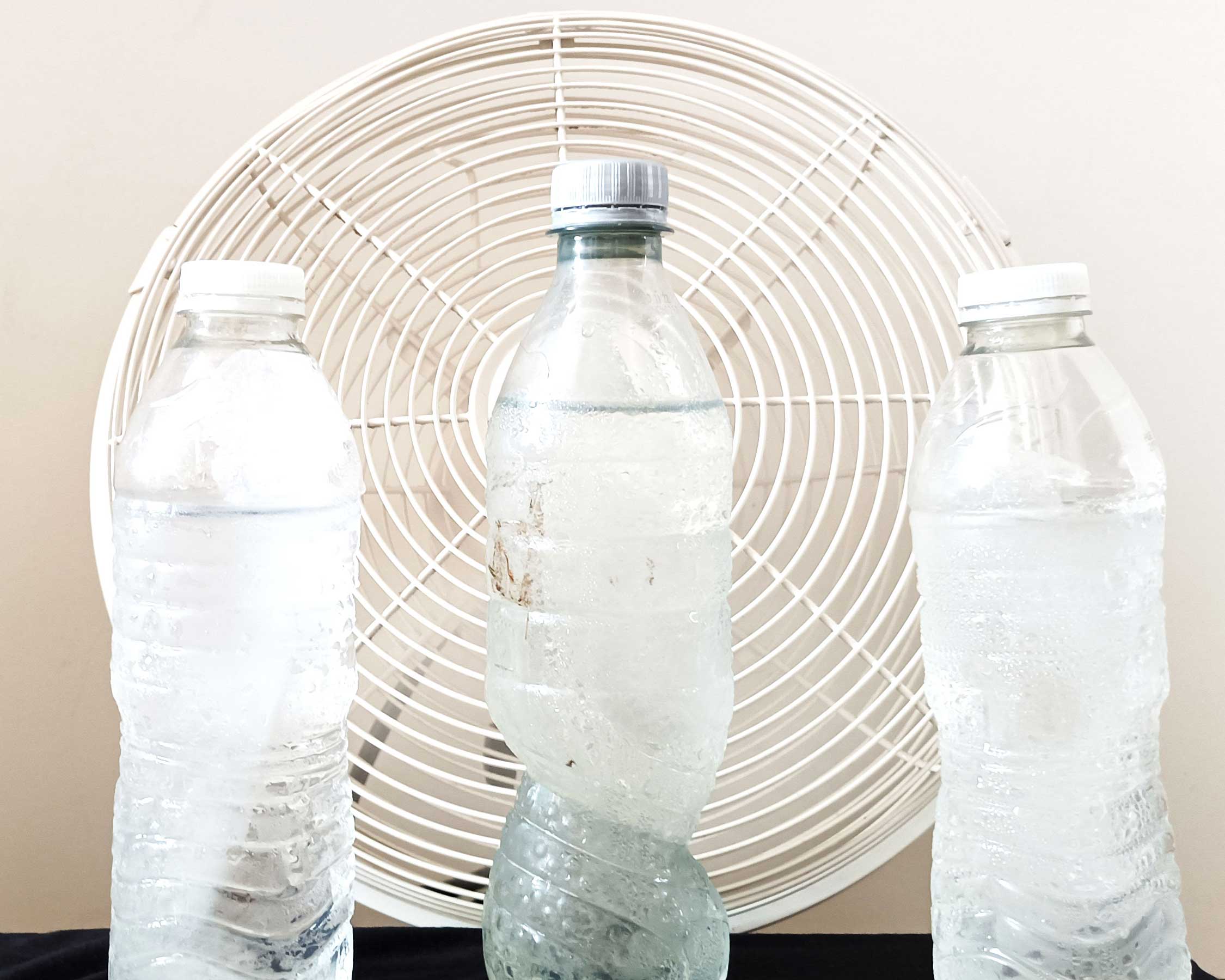 Drei Wasserflaschen in sicherer Entfernung vom elektrischen Ventilator, um den Raum zu kühlen