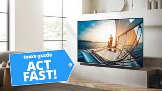 The Samsung QN90C Neo QLED TV displaying an aesthetically pleasing scene of a sailboat at sunset. The TV is in a modern living room. Overlaid on the picture is a blue badge that reads: "Tom's Guide - Act Fast!"