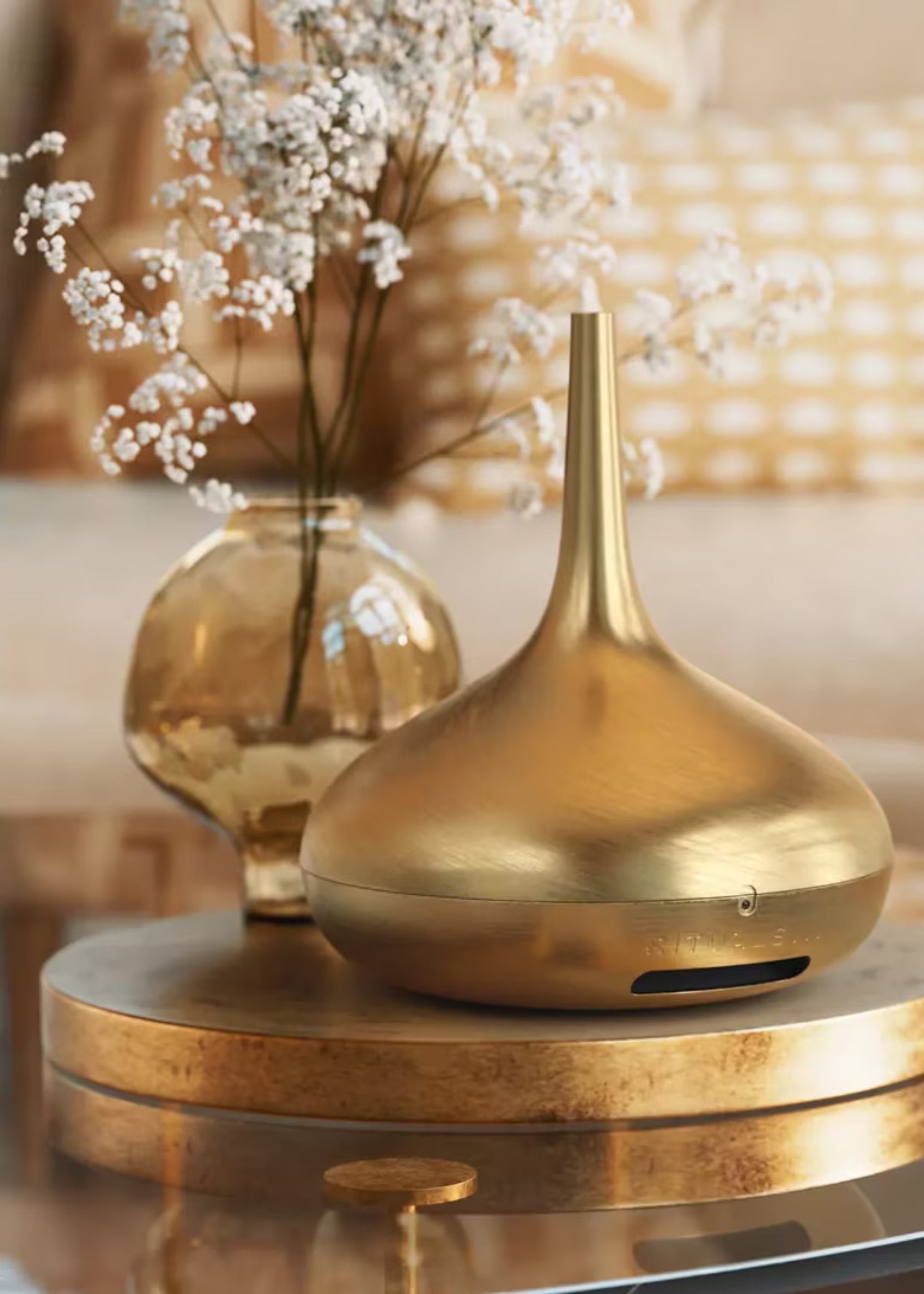A glass coffee table with a gold electric diffuser by a vase with dried flowers