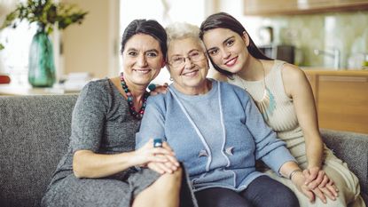 Three women of different generations in a family sit on the couch in a home.