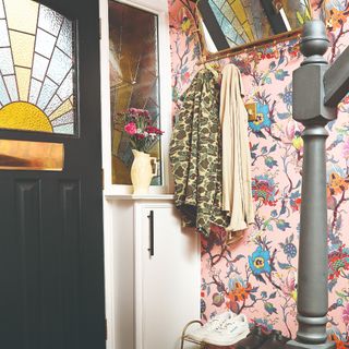 A small hallway with a pink floral wallpaper covering one wall and a black front door with a mosaic glass insert