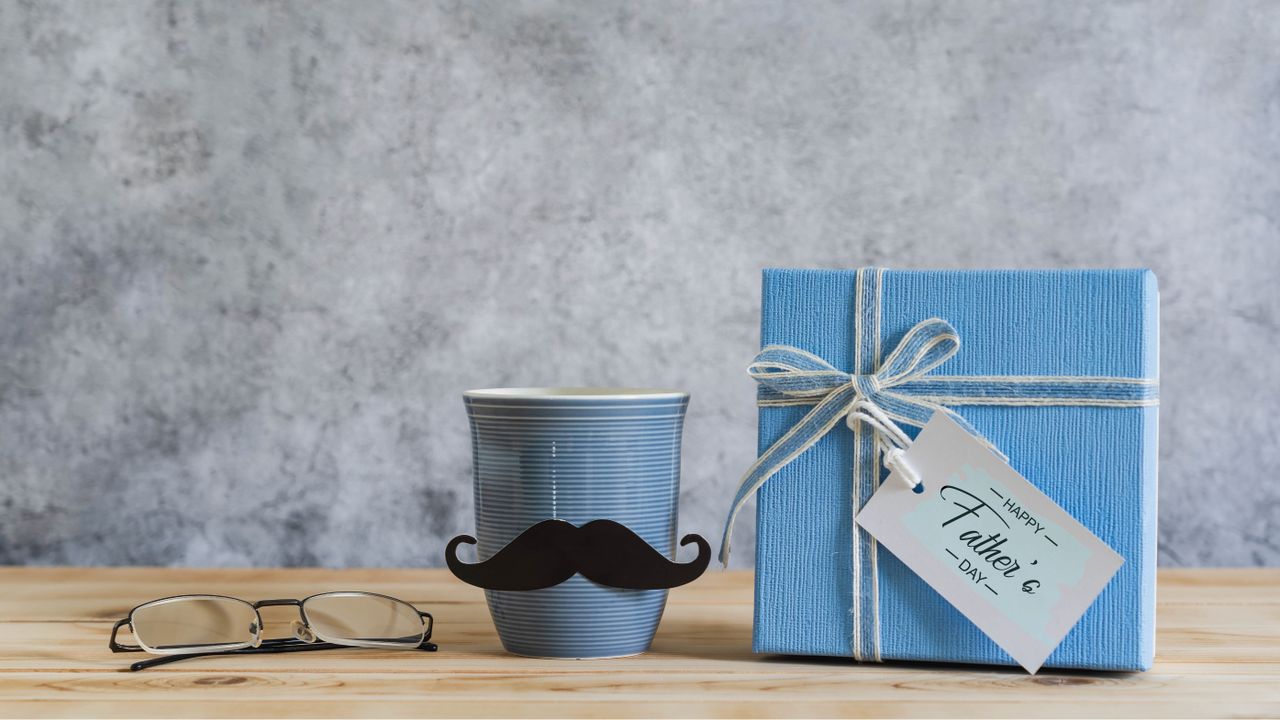 A gift box labelled Happy Father&#039;s Day beside a moustachioed cup and spectacles