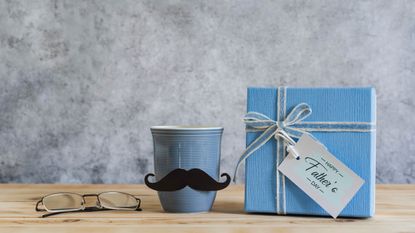 A gift box labelled Happy Father's Day beside a moustachioed cup and spectacles