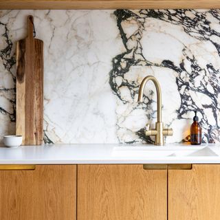 Richly veined marble kitchen splashback with white worktops and warm wood doors