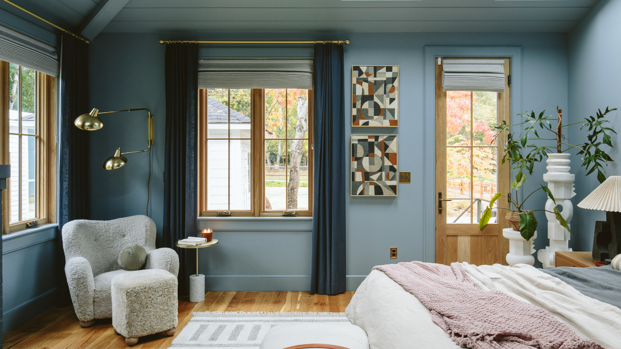 A bedroom with blue walls, a gray armchair and white plant holders.