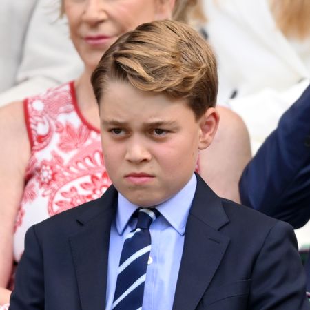 Prince George wears a navy suit with a light blue shirt and striped tie and scowls