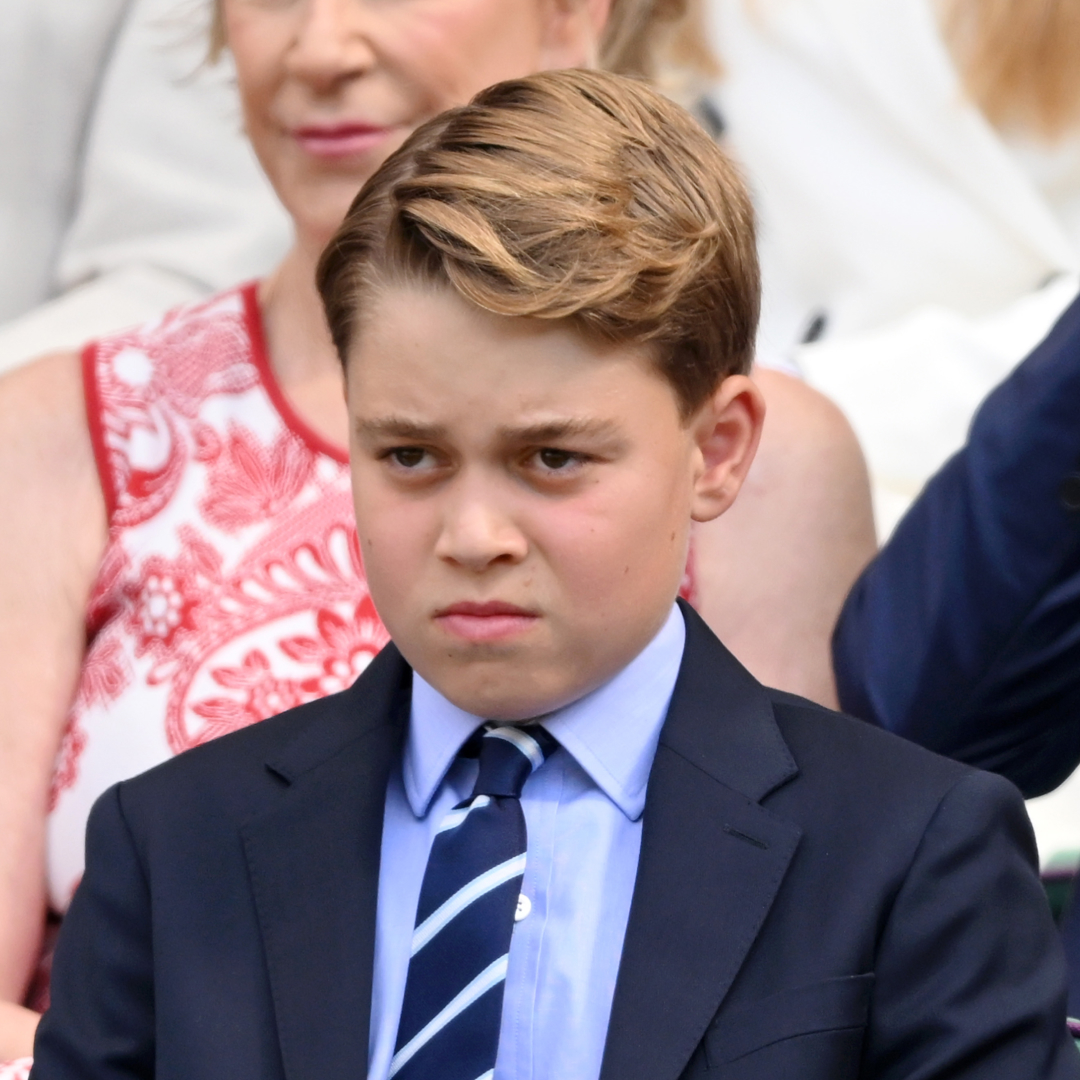 Prince George wears a navy suit with a light blue shirt and striped tie and scowls