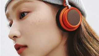 A young woman wearing a pair of orange Edifier Doo Ace headphones over a beanie