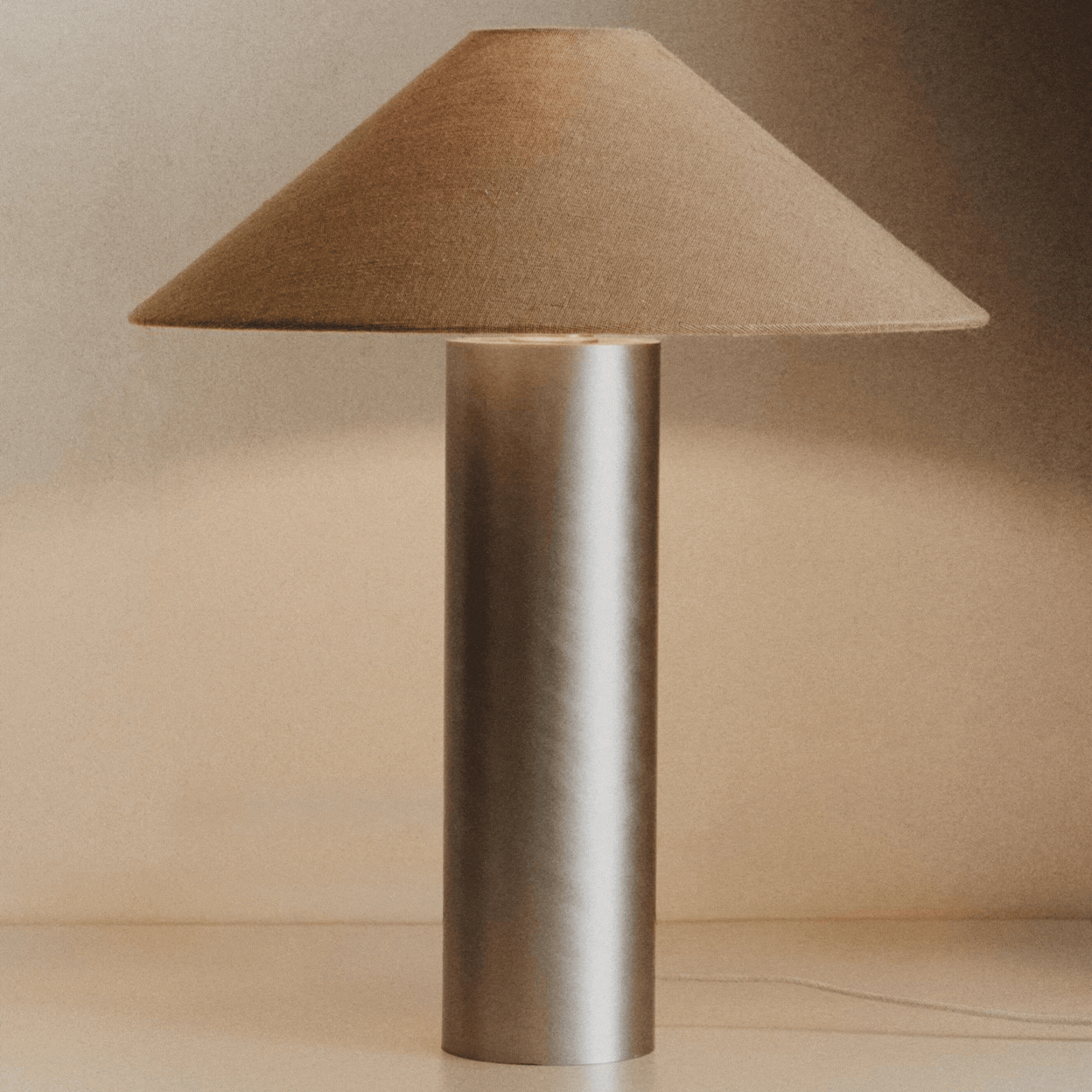 Rotating gif showing a brushed stainless steel lamp with a brown textile shade.