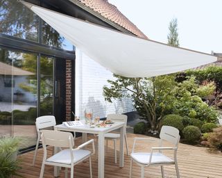 A white dining table for four on a deck with a white shade sail