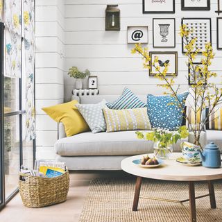 living room with white panelled wall and monochrome artwork with yellow and blue cushions on a light grey sofa