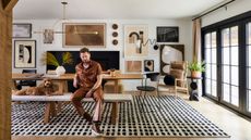 bobby berk in the dining room of his LA office, with dotted rug, gallery wall, and dining table with bench seats