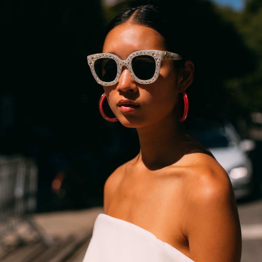 woman with bare glowing skin and sunglasses with red earrings