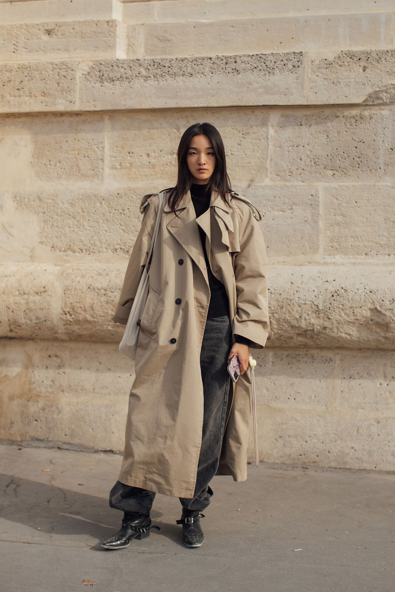 Woman wearing black moto boots, black jeans, black turtleneck, and a beige trench coat.