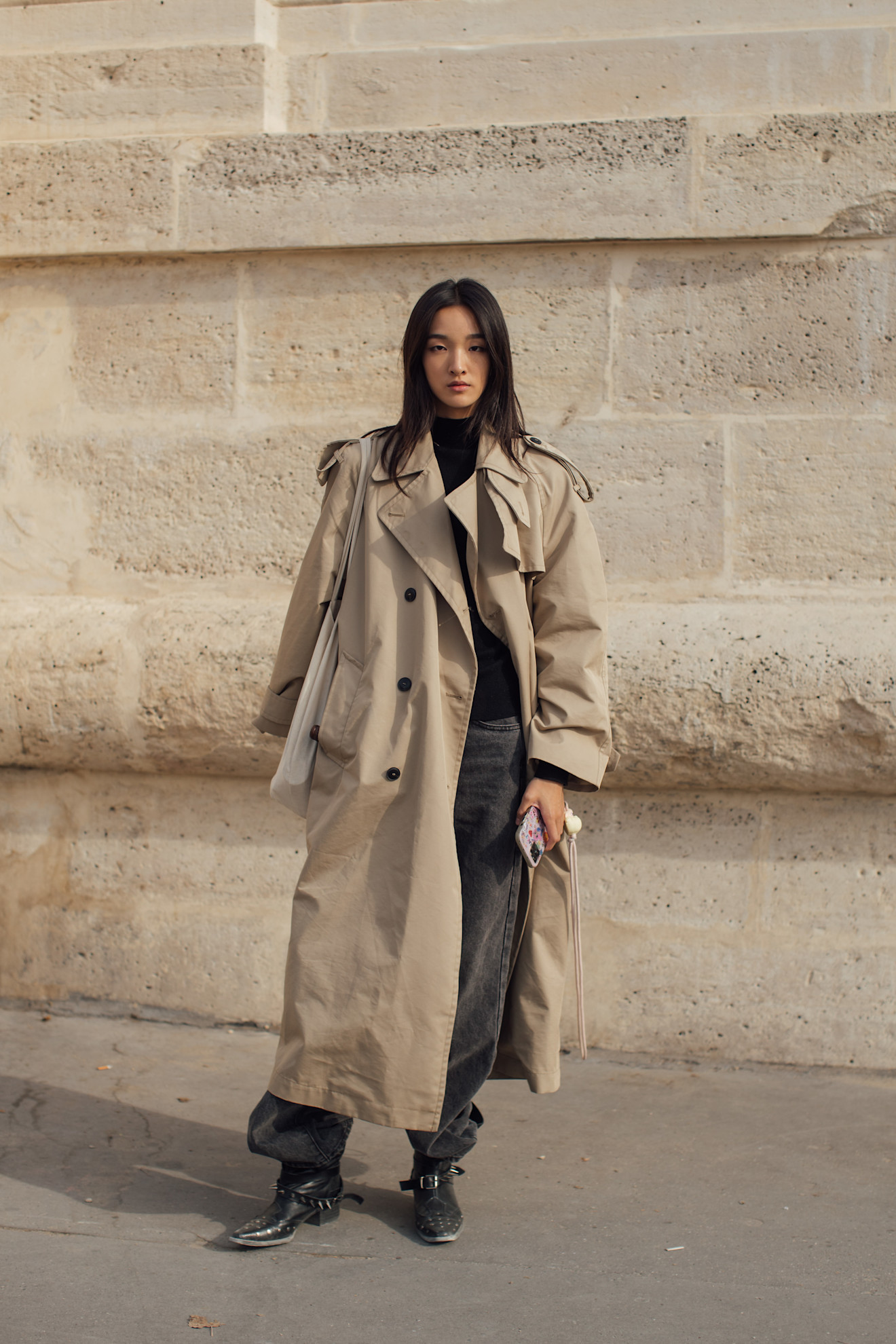 Woman wearing black moto boots, black jeans, black turtleneck, and a beige trench coat.