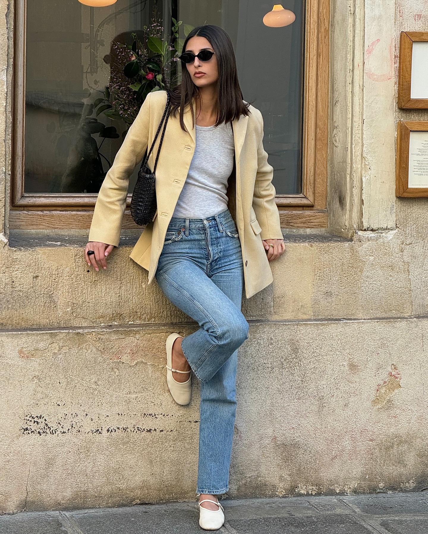 An image of an influencer wearing a beige blazer, grey T-shirt, blue jeans and cream Mary-Jane ballet flats in Paris