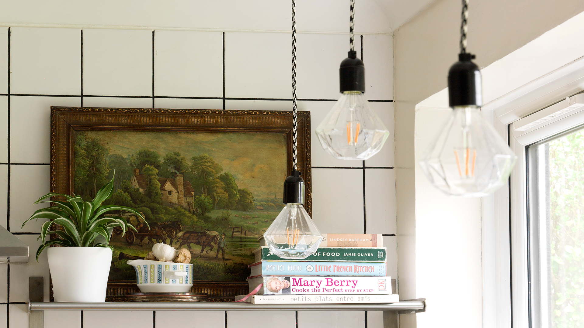 Exposed lightbulbs hanging from black and white flex in a white tiled kitchen