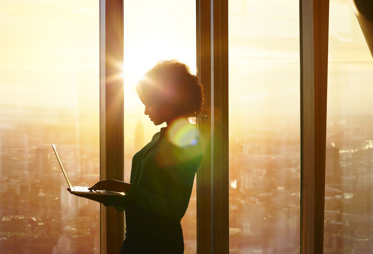 Businesswoman on laptop at window in morning sun