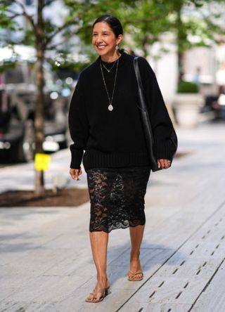 A woman in New York wearing a black oversized jumper over a lace skirt.