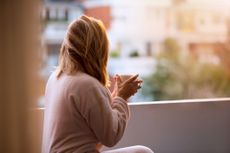 A woman drinks a cup of coffee on a balcony as the sun rises, wearing a comfortable outfit.