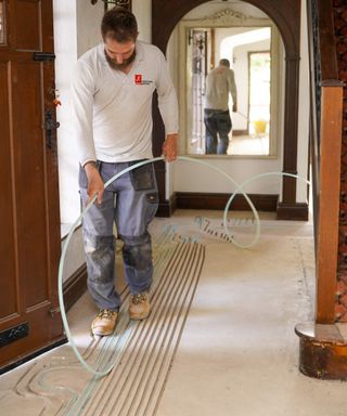 Man installing JK Floorheating's underfloor heating pipes in bespoke channels created in a concrete floor in a traditional-style hallway