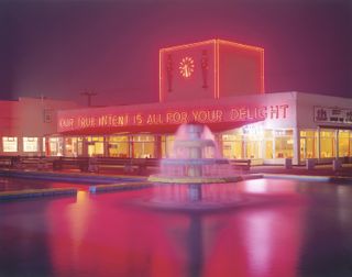 A photograph of a building with neon lights and a fountain in front of it, taken at night.